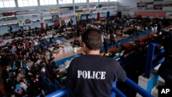 A policeman observes the scene as immigrants who arrived aboard a cargo ship from Turkey queue for meals in a basketball arena where they have been given temporary shelter in the town of Ierapetra, Crete, Nov. 28, 2014. 
