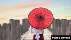 A woman in Myanmar stands under a paper umbrella.