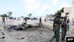 Somalian security forces walk past the remains of a car after it exploded outside Somali parliament building, Mogadishu, July 5, 2014.