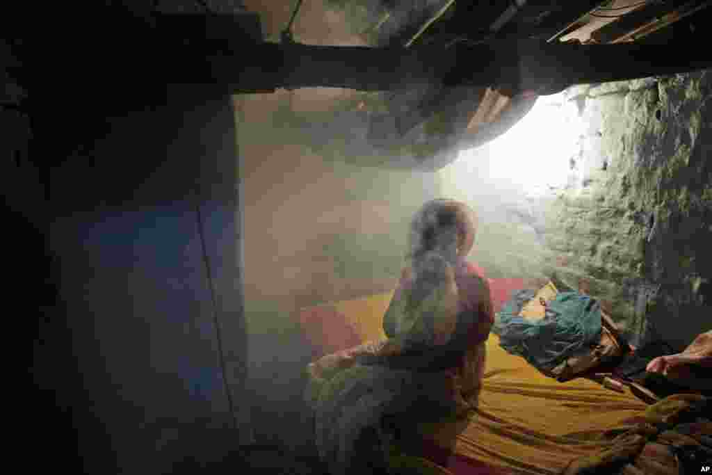 A woman sits inside her house covered with smoke from fumigation in Allahabad, India. Despite efforts, including spraying vast areas with clouds of diesel smoke and insecticide, several Indian cities battle dengue fever and other mosquito-borne diseases every year during the rainy season.