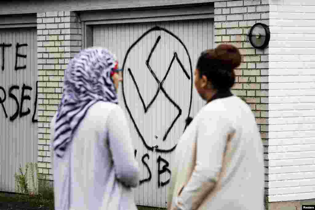 Women look at a swastika on the door of the Red Cross asylum center in Lyngbygaard, in Trustrup in the west of Denmark. The center was vandalized by unidentified men, who drew Nazi symbols and wrote a message reading "first warning" at night. A vehicle was also set on fire outside the center. 