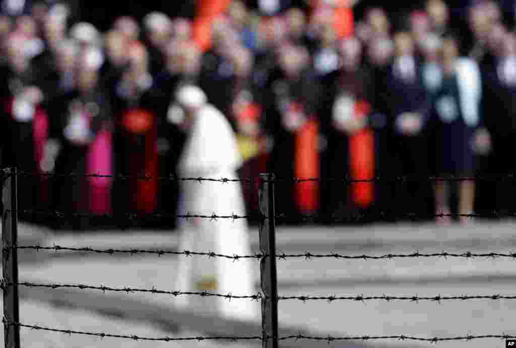 Pope Francis, background, is framed by a barbed wire as he prays in front of the memorial at the former Nazi death camp Auschwitz-Birkenau, in Oswiecim, Poland. Francis paid a somber visit to the camp Friday, becoming the third consecutive pontiff to make the pilgrimage to the place where Adolf Hitler&#39;s forces killed more than 1 million people, most of them Jews.