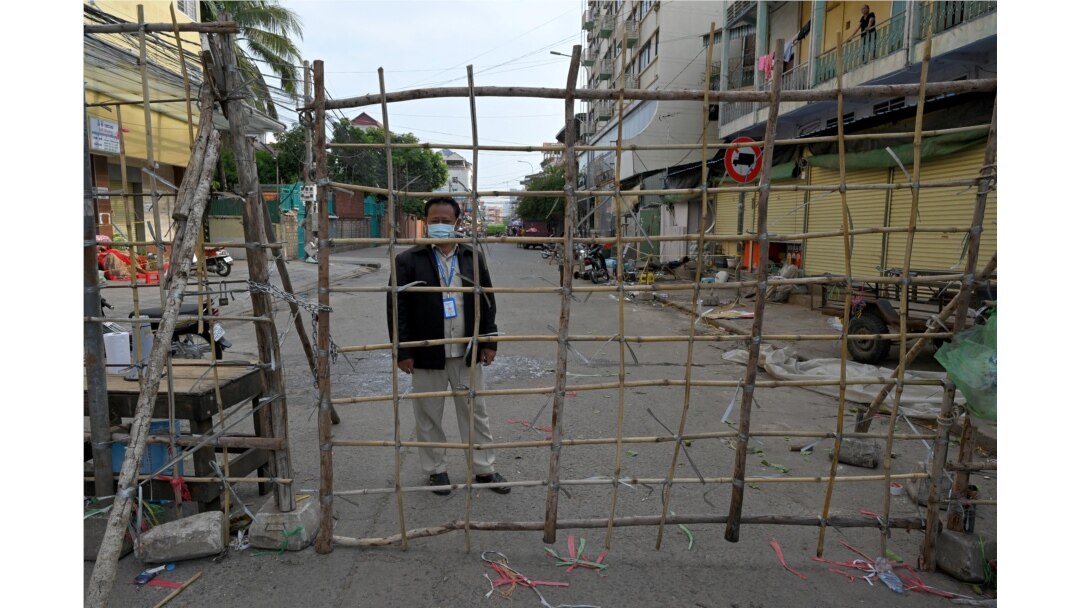 Petugas setempat berjaga di belakang barikade untuk pembatasan wilayah di tengah pandemi COVID-19 di Phnom Penh, 8 Mei 2021. (Foto: TANG CHHIN Sothy / AFP)