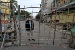 Petugas setempat berjaga di belakang barikade untuk pembatasan wilayah di tengah pandemi COVID-19 di Phnom Penh, 8 Mei 2021. (Foto: TANG CHHIN Sothy / AFP)