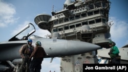 In this June 3, 2019 file photo, a pilot speaks to a crew member by an F/A-18 fighter jet on the deck of the USS Abraham Lincoln aircraft carrier in the Arabian Sea.