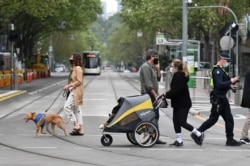 Orang-orang berjalan-jalan dengan anjing mereka di Melbourne, Australia, di tengah lonjakan infeksi COVID-19 yang mencatat 1.438 kasus, total harian terbesar sejak awal pandemi, 30 September 2021. (William WEST / AFP)