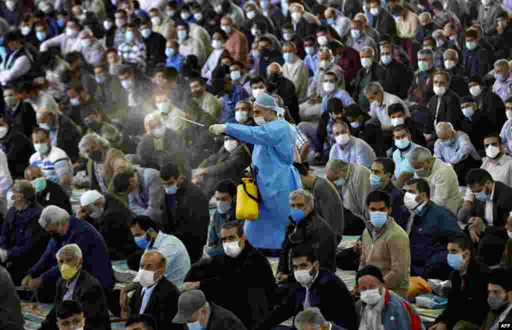 A municipal worker sprays disinfectant as mask-clad Iranians gather in a mosque in the capital Tehran to perform the Friday prayers, for the first time after authorities eased some restrictions put in place for over a year in a bid to stem the spread of COVID-19.