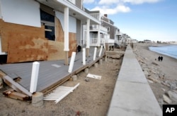 FILE - People walk along a beach near damaged beachfront homes, March 11, 2018, in Marshfield, Mass. The Northeast is bracing for its third nor'easter in fewer than two weeks.