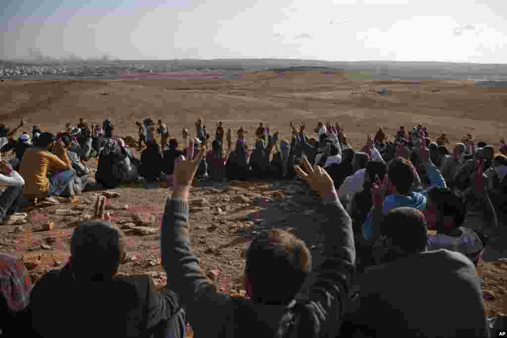 Kurdish people flash the V-victory sign&nbsp;in support of Syrian Kurd militia, on a hilltop on the outskirts of Suruc, Turkey, Oct. 15, 2014. 