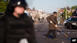 Residents clean streets as law enforcement officers stand guard, Tuesday, April 28, 2015, in Baltimore, in the aftermath of rioting following Monday's funeral of Freddie Gray, who died in police custody. (AP Photo/Matt Rourke)