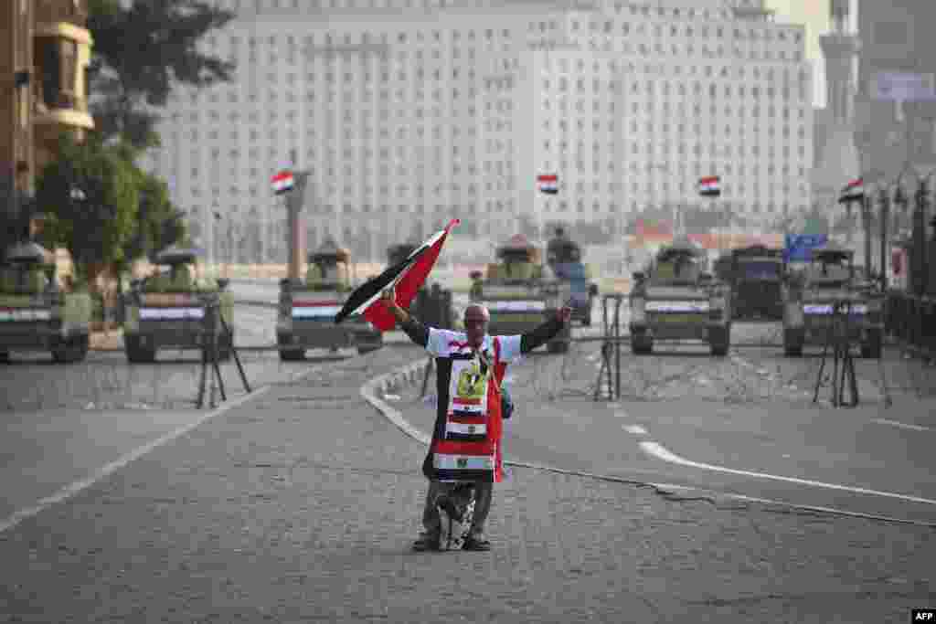 A pro-regime supporter holds Egyptian national flags in front of army vehicles positioned on Cairo&#39;s Tahrir square during a demonstration against a recent court&#39;s decision to drop a murder charge against former president Hosni Mubarak.