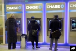 FILE - Customers use ATMs at at a branch of Chase Bank in New York, Jan. 14, 2015.