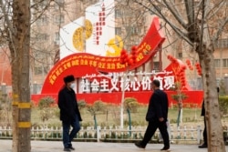 FILE - Residents walk past government propaganda, some of which reads, "Socialist core values," in Hotan in northwestern China's Xinjiang Uyghur Autonomous Region, March 22, 2021.