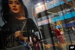 Chinese shoppers are reflected on a fashion boutique's window panels as they walk through the capital city's popular shopping mall in Beijing, Feb. 1, 2019.