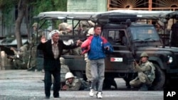 FILE - Local residents walk with their hands raised as Uzbek soldiers take positions to disperse protesters in Andijan, Uzbekistan, May 13, 2005. 