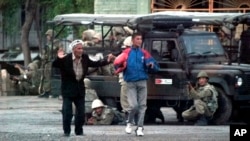 FILE - Local residents walk with their hands raised as Uzbek soldiers take positions to disperse protesters in Andijan, Uzbekistan, May 13, 2005. Several hundered people are thought to have been killed during the crackdown.