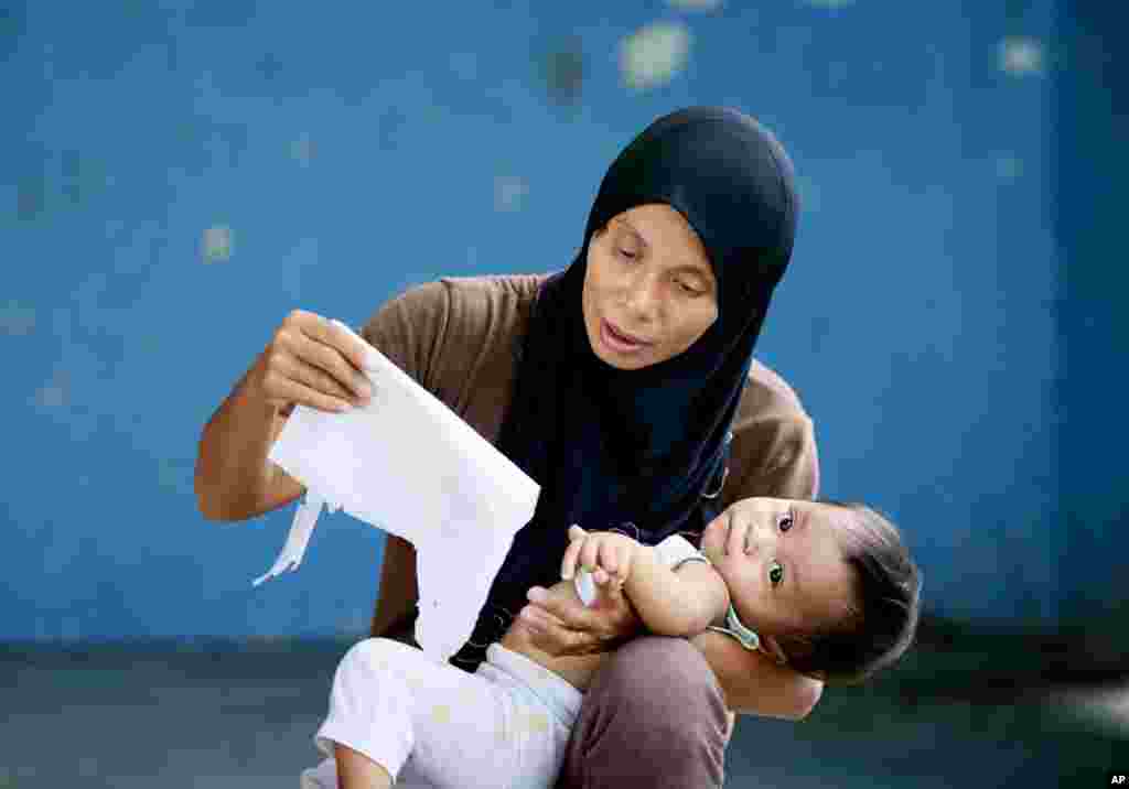 A Filipino Muslim mother cuddles her baby as she checks her name and polling precinct a day before the country&#39;s presidential elections in the front-running presidential candidate Rodrigo Duterte&#39;s hometown of Davao city in southern Philippines.