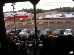 Junkers line up, rear ends facing the arena, before the start of a demo derby event at a county fair.