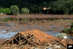 Rescue workers in a helicopter search a flooded area after a dam collapsed in Brumadinho, Brazil, Sunday, Jan. 27, 2019.