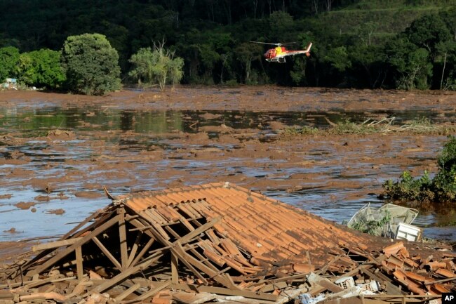 Rescue workers in a helicopter search a flooded area after a dam collapsed in Brumadinho, Brazil, Sunday, Jan. 27, 2019.