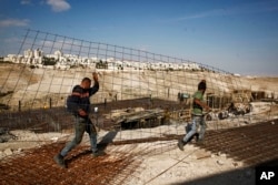 FILE - Workers carry material at a construction site in the West Bank settlement of Maaleh Adumim, Jan. 22, 2017.