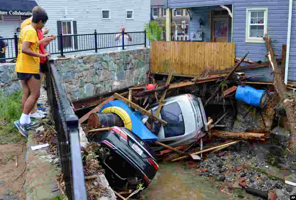 Residents gather by a bridge to look at cars left crumpled in one of the tributaries of the Patapsco River that burst its banks as it channeled through historic Main Street in Ellicott City, Maryland.