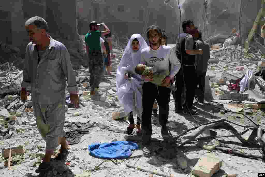 A Syrian family walks amid the rubble of destroyed buildings following a reported airstrike in the Bustan al-Qasr rebel-held district of Aleppo, April 28, 2016. A Syrian monitoring group and a team of first-responders say new airstrikes on the rebel-held part of the contested city of Aleppo have killed over a dozen people and brought down at least one residential building.