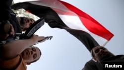 A boy holding a weapon stands under a Yemeni national flag, as followers of the Houthi group demonstrate against an arms embargo imposed by the U.N. Security Council on the group in Sanaa, April 16, 2015.