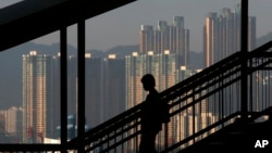 FILE - A woman walks down a stairway against the backdrop of high-rise apartment buildings in Hong Kong.