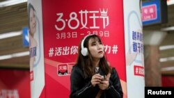 Seorang perempuan berdiri di depan iklan platform e-commerce Alibaba, di stasiun kereta bawah tanah di Beijing, Cina 7 Maret 2018. (Foto: REUTERS/Jason Lee)