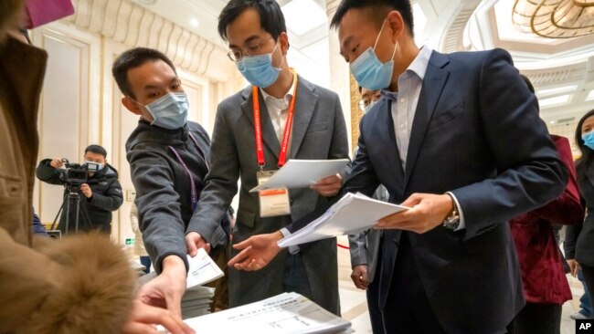 FILE - Journalists reach for copies of a Chinese government-produced report titled "Democracy That Works" at the State Council Information Office in Beijing, Dec. 4, 2021. China's Communist Party took American democracy to task that day, sharply criticizing a global democracy summit to be hosted by President Joe Biden and extolling the virtues of its governing system.