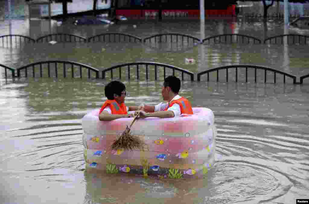 Men sit in an inflatable tub along a flooded street as heavy rainfall hits Lishui, Zhejiang province, China, Aug. 20, 2014.