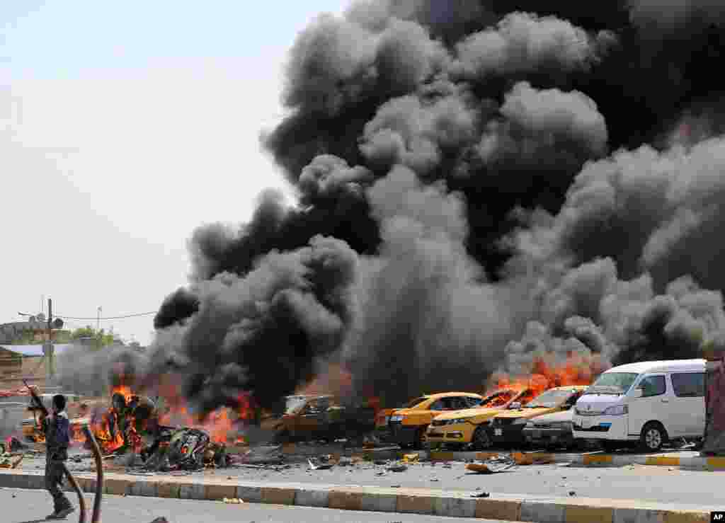 An Iraqi policeman stands near burning vehicles moments after one in a series of bombs hit the Shi&#39;ite stronghold of Sadr City, in Baghdad, Iraq, killing tens.