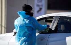 FILE - A medical technician performs a nasal swab test on a motorist queued up in a line at a COVID-19 testing site near All City Stadium, Dec. 30, 2021, in southeast Denver.