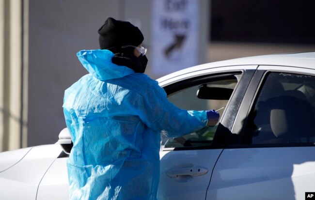 FILE - A medical technician performs a nasal swab test on a motorist queued up in a line at a COVID-19 testing site near All City Stadium, Dec. 30, 2021, in southeast Denver.