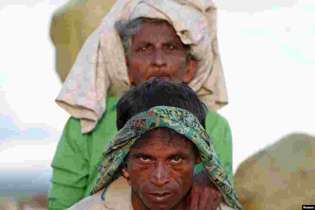 Arakanlı Müslümanlar yaşlıları sırtlarında taşıyarak pirinç tarlalarını geçiyor.