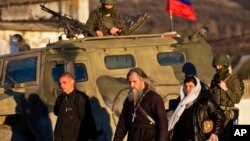 Archbishop Clement of Ukrainian Orthodox Church, center, walks past a pro-Russian armored vehicle, soldiers, Ukrainian military base, Perevalne, March 15, 2014.