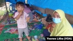 Ibu Rida (baju kuning) saat berada di tenda terpal yang didirikan di depan rumahnya yang rusak berat akibat gempa di desa Kayuangi, Kecamatan Malunda. Jumat (28/1/2021). (Foto: VOA/Yoanes Litha)