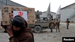 FILE - An Afghan man carries an aid package he received at a distribution site in Kabul, Afghanistan, Dec. 15, 2021, as Taliban fighters stand in the background.