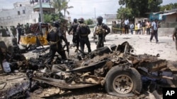 Somali soldiers stand near the wreckage of a car used in a suicide car bomb attack outside the Criminal Investigation Department (CID) in Mogadishu, Somalia, July 31, 2016.