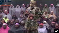 FILE- In this undated image taken from video distributed Sunday, Aug. 14, 2016, an alleged Boko Haram soldier standing in front of a group of girls alleged to be some of the abducted Chibok schoolgirls held since April 2014.