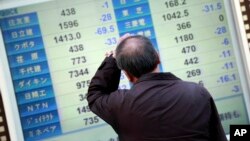 A man scratches his head as he looks at an electronic stock board showing Japan's Nikkei 225 in Yokohama, near Tokyo, Wednesday, Feb. 10, 2016.