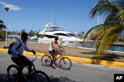 People cycle past U.S. yacht Still Water, moored at Hemingway Marina in Havana, Cuba, Thursday, Aug. 6, 2015.