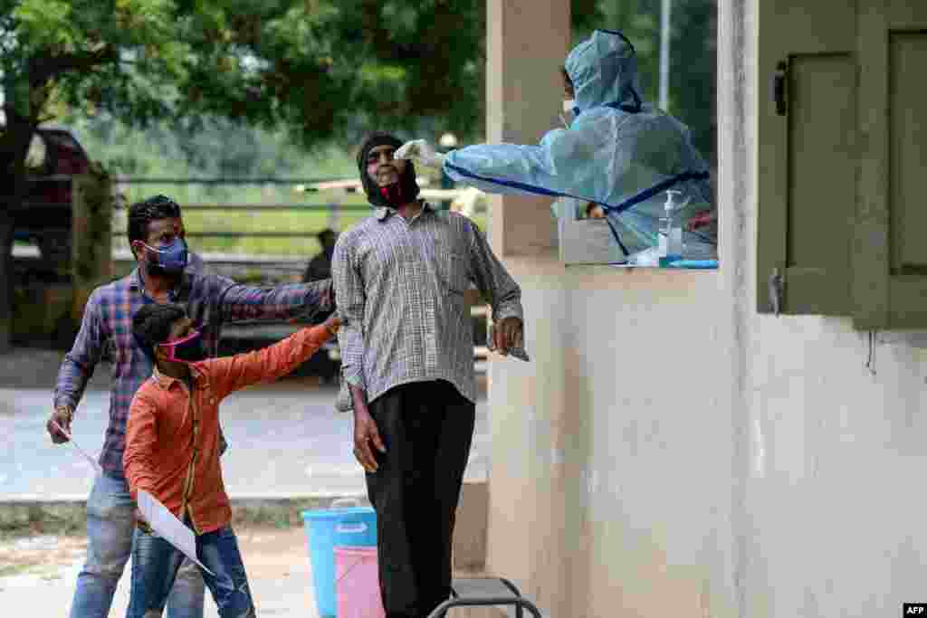 Locals hold a man as a health worker collects a sample from him to test for COVID-19 at a community center on the outskirts of Hyderabad, India.
