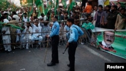 Policemen stand guard near supporters of the Pakistan Muslim League - Nawaz (PML-N) party during an election campaign rally in Islamabad, May 5, 2013.