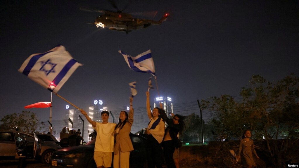 La gente ondea banderas israelíes mientras un helicóptero, que transportaba rehenes liberados como parte de un acuerdo entre Israel y el grupo islamista palestino Hamás, sale del Centro Médico Infantil Schneider en Petah Tikva, Israel, el 24 de noviembre de 2023.