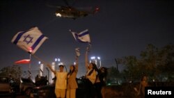 La gente ondea banderas israelíes mientras un helicóptero, que transportaba rehenes liberados como parte de un acuerdo entre Israel y el grupo islamista palestino Hamás, sale del Centro Médico Infantil Schneider en Petah Tikva, Israel, el 24 de noviembre de 2023.