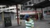 Un hombre con un tapabocas camina frente a una estación de servicio de una compañía petrolera estatal vacía mientras un camión cisterna descarga gasolina en Caracas.