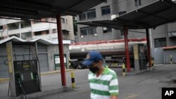 Un hombre con un tapabocas camina frente a una estación de servicio de una compañía petrolera estatal vacía mientras un camión cisterna descarga gasolina en Caracas.