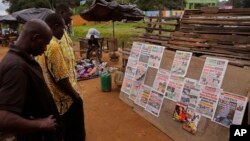 Men read newspaper headlines after recent elections near the entrance to the local zoo, right rear, in Abidjan, Ivory Coast, Monday, Oct. 26, 2015.